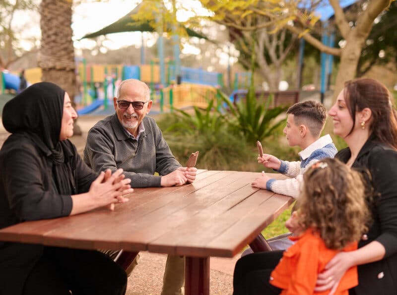 An Arabic family chatting and eating ice creams at a park table.